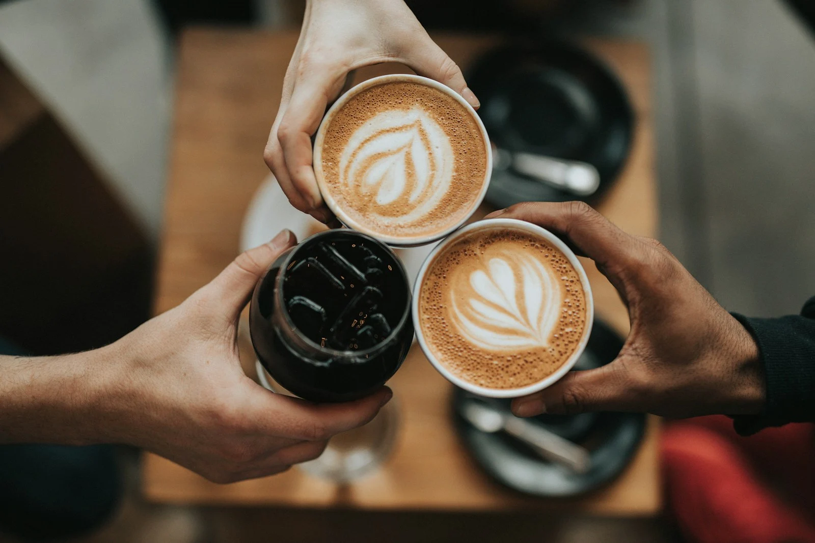 Three adults holding coffee cups together; hands only