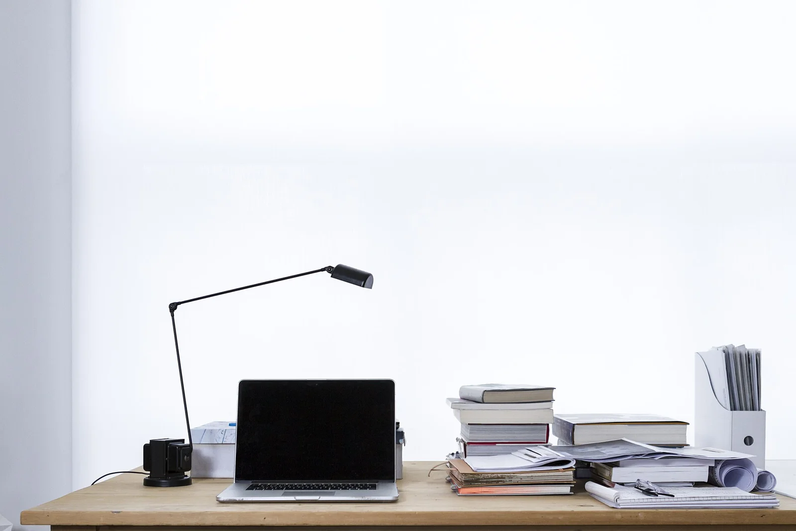 Laptop on desk book stacks (Unsplash)
