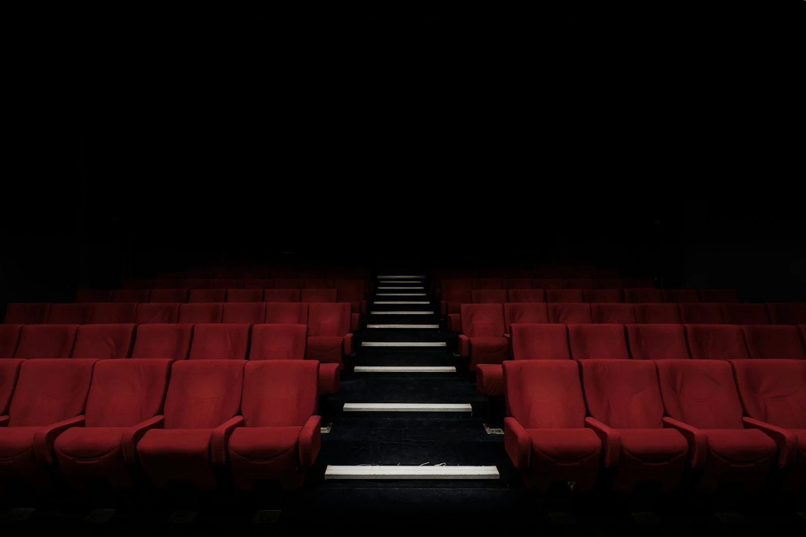 Empty cinema auditorium with red seats and an illuminated centre aisle